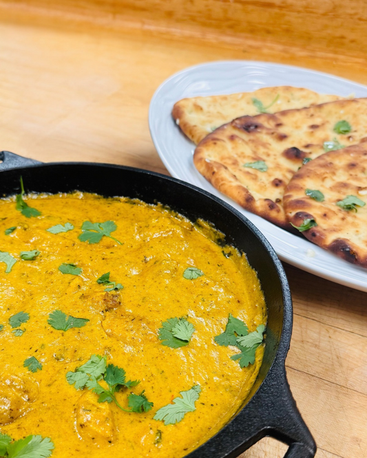 CARINARA Butter Chicken in a creamy orange sauce over rice, garnished with cilantro with a side of naan