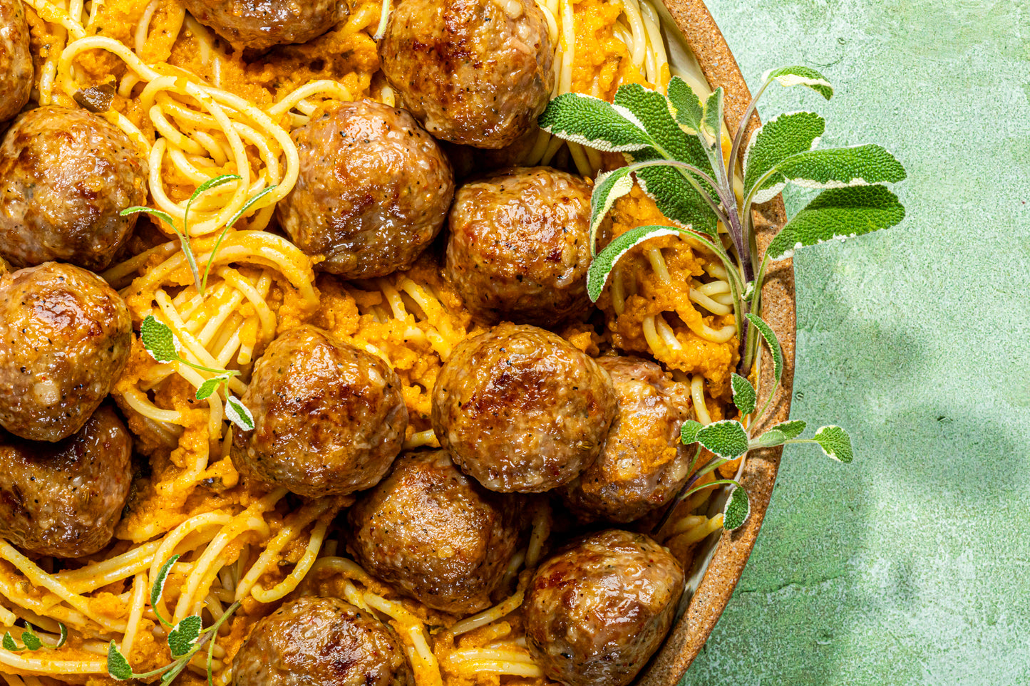 A close up image of spaghetti and meatballs prepared with CARINARA pasta sauce in a bowl with fresh sprigs of oregano as garnish all set on a light green stone background.